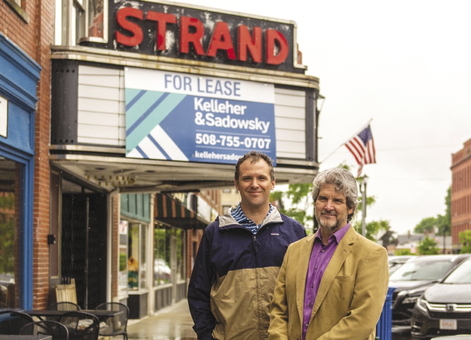 Two men stand in front of The Strand theater marquee in Clinton.